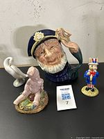 View of all four figurines including Royal Doulton Old Salt jug, Uncle Sam Bunnykins, Lladro bird, and Italian putti figurine.