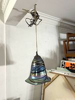Full view of vintage hanging pendant lamp with iridescent bell-shaped art glass shade and cord hanging from ceiling fixture.