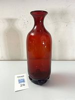 Full view of tall red hand-blown glass bottle with visible raspberry prunts at the base.