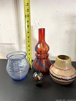 Four vintage European vases on black surface with measuring tape behind showing 10-inch height for tallest vase