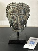Front view of bronze Buddha head sculpture with coiled curls and serene expression on black stand.