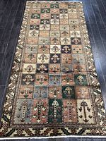 Full view of Bakhtiar Persian rug laid flat on dark hardwood floor, showing full panel grid pattern and decorative border.