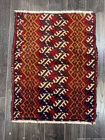 Full view of the Arak hand-knotted Persian rug laid flat on dark wooden flooring, showcasing geometric red, orange, black, and cream pattern.