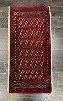 Full view of rectangular Torkman rug showing red base color with geometric diamond pattern and bordered edges