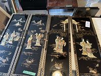 Four long narrow panels, black lacquered with 3D Asian figures and gold decoration.