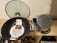 Cast iron wok with glass lid, steamer insert, and cooking utensils laid out on table