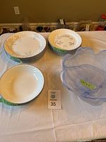 Stack of Corelle dishes with pink floral pattern and one chipped plate, along with blue glass bowl on table.