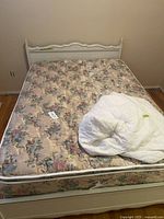Wooden white bed frame with floral mattress and white mattress protector on top, showing overall lot contents.
