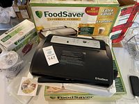 Two boxed FoodSaver V2830 vacuum packaging systems, one unboxed showing buttons and control panel.