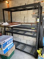 Front view of assembled shelving unit in garage showing five wire-mesh shelves supported by black steel posts