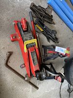 Top-down view of all items including one red hydraulic jack, two black scissor jacks, two black stands, and two tire irons
