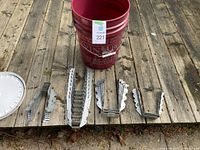 Collection of galvanized steel joist hangers laid out in front of a red bucket showing a variety of sizes and shapes.
