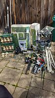 Shows full lot items including iron candle holder stakes in box, garden tools, feeder bottles, plant brackets, watering tools, garden decor figures, outdoor power post boxes, small folding metal shelf