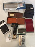 Photo showing all items: five wallets in various materials and colors, key fobs, card holder, and large boxed cutting knife.