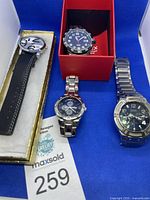 Four men's watches arranged on a blue cloth, showing different dial styles and bracelet types to identify the lot contents.