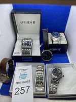 Lot of six men's watches displayed with some in original boxes (Gruen II, Benrus) and others laid out, showing various brands and styles including leather and metal bands.