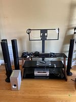 Front view showing four tall black speakers, grey subwoofer, black DVD player and receiver on a glass TV stand with audio cables on top