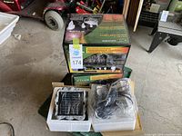 Three boxed sets of Solar e-CLIPS Outdoor Multi-Use Solar Perimeter Lighting. One box is open displaying components including LED lights, solar power rock, screws, and rechargeable battery, all in foam packaging.