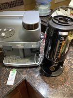 Silver Spidem Trevi espresso machine with control knobs, integrated bean hopper on top, next to black Zojirushi Movenpick coffee dispenser on countertop.