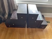 Side view of two stepped storage drawer units side-by-side showing multiple drawers and knobs, dark brown wood finish