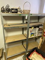 Two metal frame storage shelves positioned side by side, showing overall condition and shelving surfaces with some small items on top.