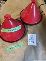 Photo of two red ceramic tagine cookers with black base rims and conical lids, labeled with dimensions 8.5 x 8.5 inches.