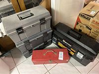 Photo of four assorted tool boxes including two stacked gray plastic tool boxes, one black Bostitch plastic tool box, and one red metal tool box with latch and handle.