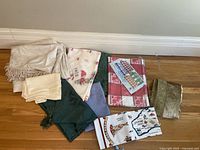 Photo of assorted table linens including valance, napkins, tablecloths, and runners laid out on the floor.