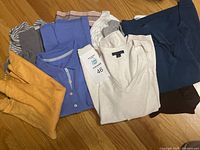 Photo showing 8 tops folded and laid out in different colors including yellow, blue, white, grey, and stripes.