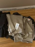 Pile of clothing including beige blazer and pants, dark knit sweaters and other garments