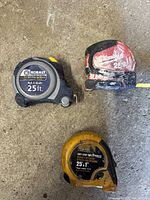 Three tape measures from Kobalt, Milwaukee, and Husky brands displayed on concrete surface showing condition and markings.