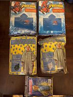 Top view photo showing two children's Marvel Spider-Man ponchos and two adult gray hooded ponchos in yellow packaging, all new.