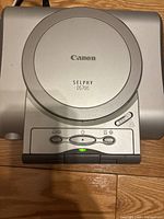Close-up front view of Canon Selphy DS700 printer showing circular top, brand, model, and control buttons with indicator light on.