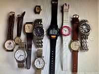 Full view of 11 assorted watches arranged in two rows showing variety of dial styles, bands, and colors.