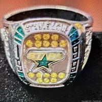 Close-up photo of the ring face showing yellow stones, Dallas Stars logo, and green accents