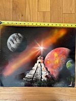 Full view of the painting with a measuring tape showing approximately 15 inches width. Cosmic scene with planets, starburst, and pyramid structure.