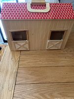 Closed wooden horse stable showing front with two hinged doors beneath windows, cream wood paneling and red roof tiles pattern, with cream carry handle on top.