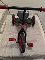 Front view of red and black Ruff n' Tuff three-wheeled tricycle showing pedals, seat, and handles.