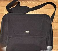 Black laptop bag laid flat showing front flap pocket and shoulder strap.