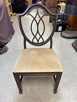 Front view of one dark wood traditional dining chair with beige upholstered seat and carved shield back.