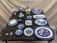Full overhead view of all Delftware items laid out on table, showing variety of plates, platters, teapot, vase, oil lamp, cup and salt and pepper shakers.