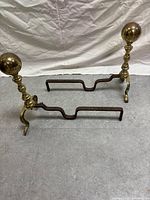 Pair of antique fireplace andirons, showing brass uprights with spherical finials and rusted iron horizontal bars.