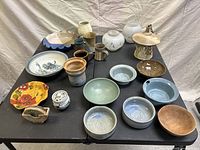 Top view of multiple artisan-style pottery pieces and bowls arranged on a black folding table against a fabric backdrop.