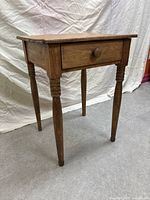 Side angle view of rustic wooden bedside table showing drawer and turned legs