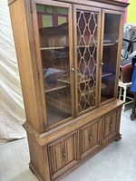 Front view of vintage wooden buffet and hutch china cabinet showing three upper glass doors with lattice pattern on the center door and three lower cabinet doors with raised panels and brass pulls.