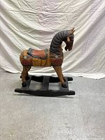 Side view of the wooden rocking horse showing detailed carving, painted body and legs, black mane, and rockers.
