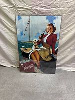 Full frontal view of the Coca-Cola poster showing woman holding bottle and dog on boat with sea and sky background.