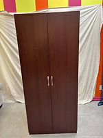 Front view of double-door dark brown MDF wardrobe against colorful wall and beige backdrop.