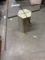 Hexagonal glass top seen from top angle, showing clear glass and brass metal supports, resting on hollowed hexagonal stone pedestal base.