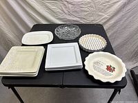 Assorted serving and baking dishes arranged on black table showing plate stacks, glass dish, and ceramic dishes with decorative patterns.